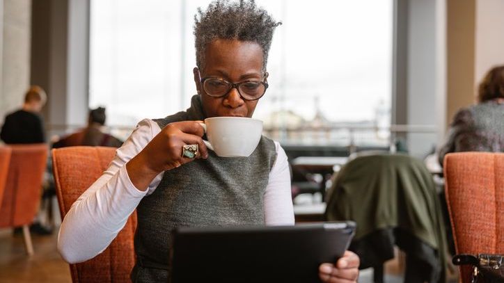 A woman who's still working fulltime looks over her Social Security benefits on her laptop. while sipping a cup of coffee. 