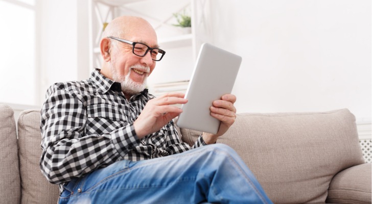 A man who appears to be in his 60s smiles while using a tablet. 